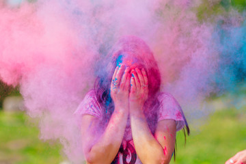 Young woman stands in colorful splashes or clouds of holi powder