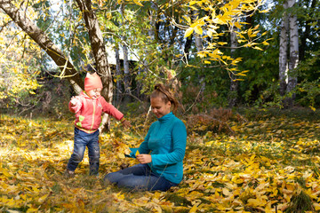 Fototapeta premium Mom and baby in the park on the background of autumn foliage