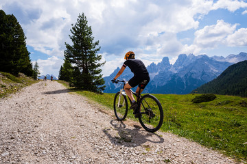Fototapeta premium Tourist cycling in Cortina d'Ampezzo, stunning rocky mountains on the background. Woman riding MTB enduro flow trail. South Tyrol province of Italy, Dolomites.
