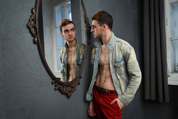 A young male hipster is reflected in a mirror in a carved frame.