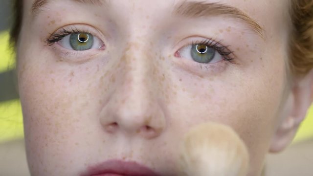 Close up of female face with freckles and brush putting blusher on cheekbones