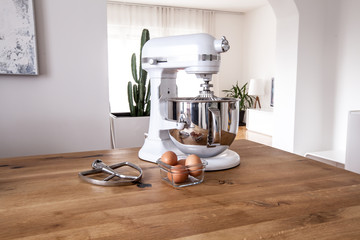 White kitchen machine and stand mixer on a wooden table in a bright design apartment
