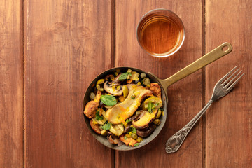 A photo of a rustic mushrooms and olives saute in a cast iron pan, with a glass of white wine, shot...
