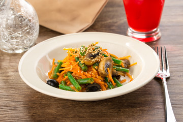 Cooked green beans with carrot and sesame seeds in a white plate on wooden table