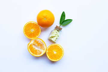 Vitamin C bottle and pills with orange fruit on white