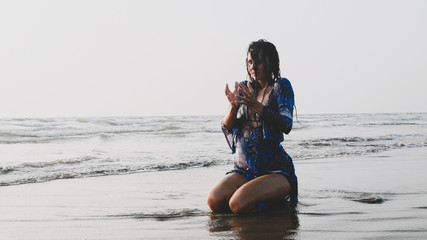 Fototapeta na wymiar Attractive wet woman sitting in water at sandy beach and doing meditation practices