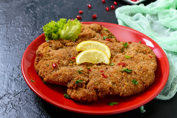 Large Viennese schnitzel on a red plate with lemon on a black background. Meat dish.