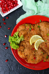 Large Viennese schnitzel on a red plate with lemon on a black background. Meat dish. Top view, flat lay.