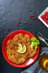 Large Viennese schnitzel on a red plate with lemon on a black background. Meat dish. Top view, flat lay.