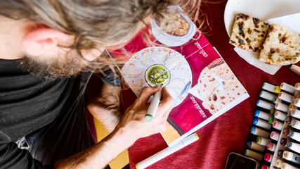 Male artist sits in cafe and drawing image of Indian food in sketchbook by art markers, close-up.