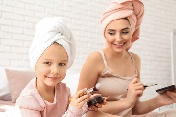 Cute little daughter and her mother doing makeup at home