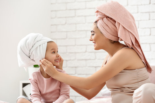 Cute little daughter with her mother after shower sitting on bed