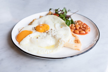 Delicious English breakfast with two fries eggs, beans, and salad on marble table.