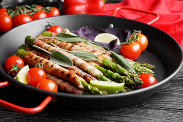 Pan with bacon wrapped asparagus on wooden table