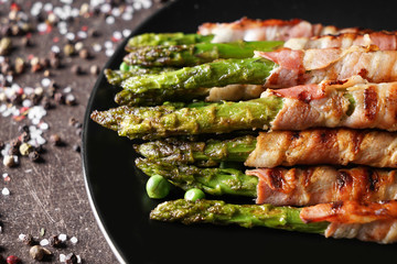 Plate with bacon wrapped asparagus on grey table, closeup