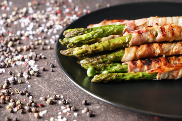 Plate with bacon wrapped asparagus on grey table, closeup