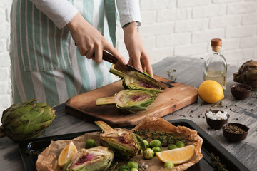 Woman preparing tasty raw artichokes in kitchen