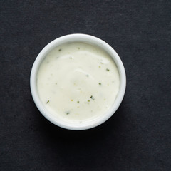 Bowl of sour cream dip sauce with herbs on the black background