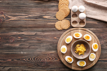 Board with hard-boiled cut eggs, yolk and waffles on wooden table