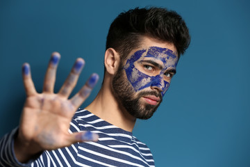 Portrait of handsome man with paint on his face and hand against color background