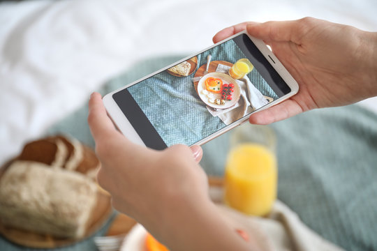 Female food photographer with mobile phone taking picture of tasty breakfast at home, closeup