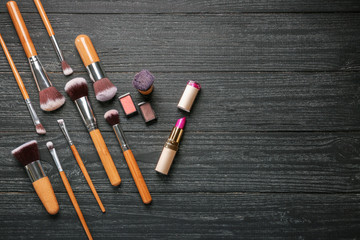 Professional makeup brushes with cosmetics on wooden background