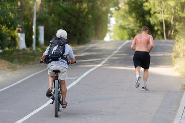 Obraz premium elderly woman riding a bicycle, young man with a naked torso running, playing sports outdoors