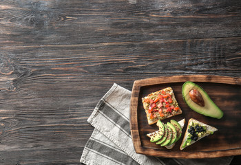 Board with tasty avocado sandwiches on wooden table