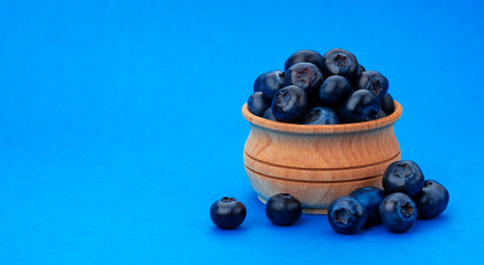 Blueberry isolated on blue background with copy space. A pile of fresh blueberries in a wooden bowl