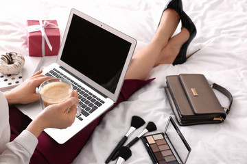 Young businesswoman with laptop drinking coffee on bed in morning