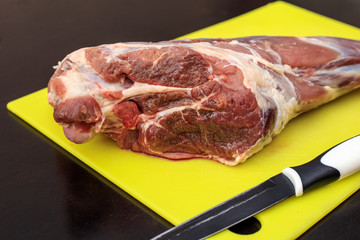 Raw meat, lamb leg on a bright color cutting board, on a dark background