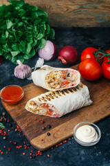 Doner kebab (shawarma or doner wrap). Grilled chicken on lavash (pita bread) with fresh vegetables - tomatoes, green salad, peppers. Old wooden background. Middle Eastern food, arabic fast food