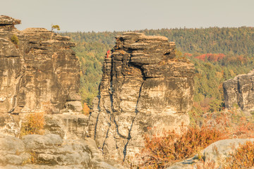 Elbe sandstone mountains in Saxony with the Bastei in autumn with mountaineers in the sunshine. Rock formation and trees are illuminated by the autumn sun.