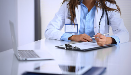 Unknown doctor woman filling up medical form while sitting at the desk in hospital office. Physician at work. Medicine and health care concept