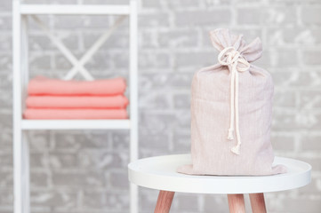 On the background of a gray brick wall stands a bedside table in which lies a stack of living coral plaids. Next is a bag with a gift.