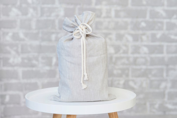 On the background of a gray brick wall there is a tabouret on which there is a bag with a gift
