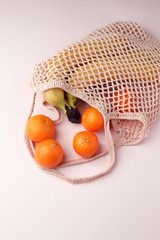 Fresh raw tangerine and banana in string bag on pastel pink background. Flat lay, top view summer, organic food, blogger style concept