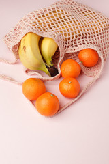 Mesh shopping bag with exotic fruits on pink canvas background. Summer time blogger organic food concept, minimal