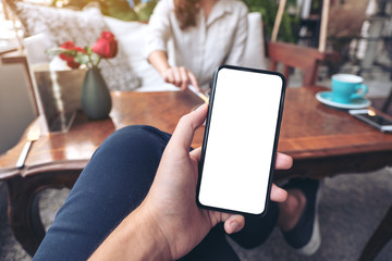 Mockup image of a man's hand holding black mobile phone with blank white screen with woman sitting in cafe