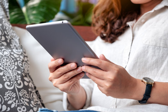 Closeup image of a beautiful asian woman holding and using tablet pc while sitting on sofa
