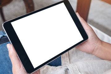 Mockup image of a woman's hands holding black tablet pc with blank white screen horizontally while sitting in cafe