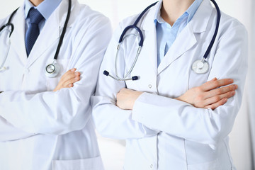 Team of unknown doctors standing straight with arms crossed in hospital. Physicians ready to help. Healthcare, insurance and medicine concept