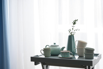 Ceramic cups with teapot on table near window