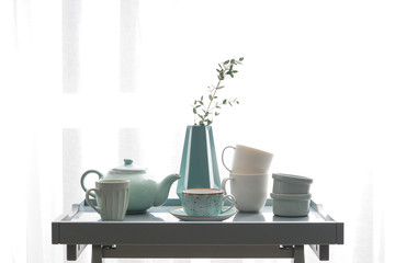 Ceramic cups with teapot on table near window