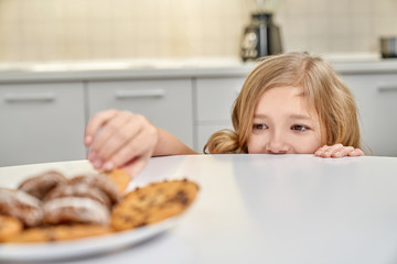 Child secretly taking american cookies from plate.