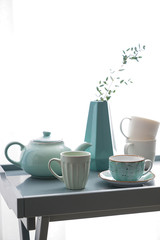 Ceramic cups with teapot on table near window
