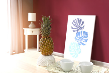 Pineapple with cups on table in interior of room