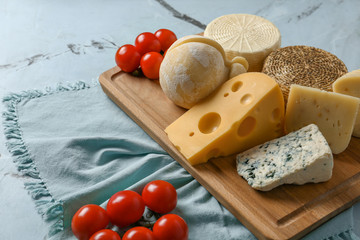 Wooden board with assortment of tasty cheese on table