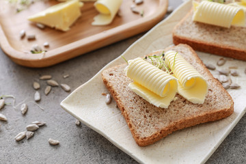 Plate with tasty butter and bread on grey table