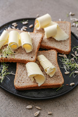 Plate with tasty butter and bread on grey table